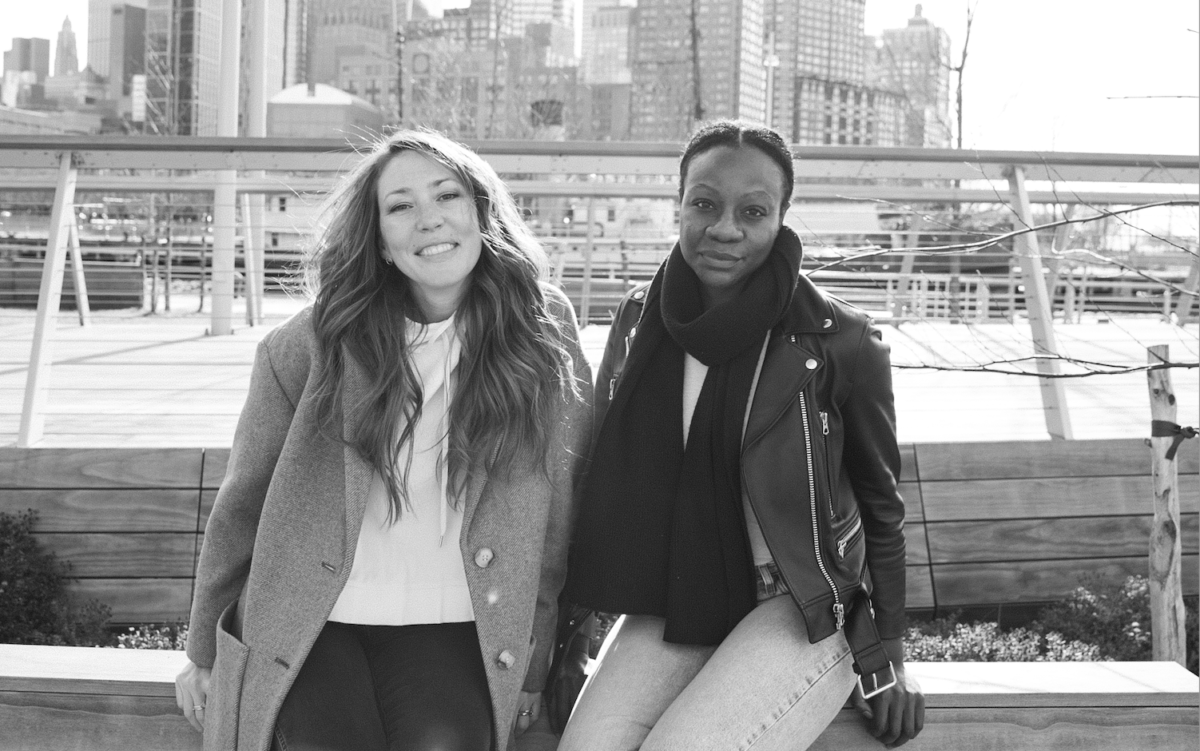 Two women in front of river with city skyline in background